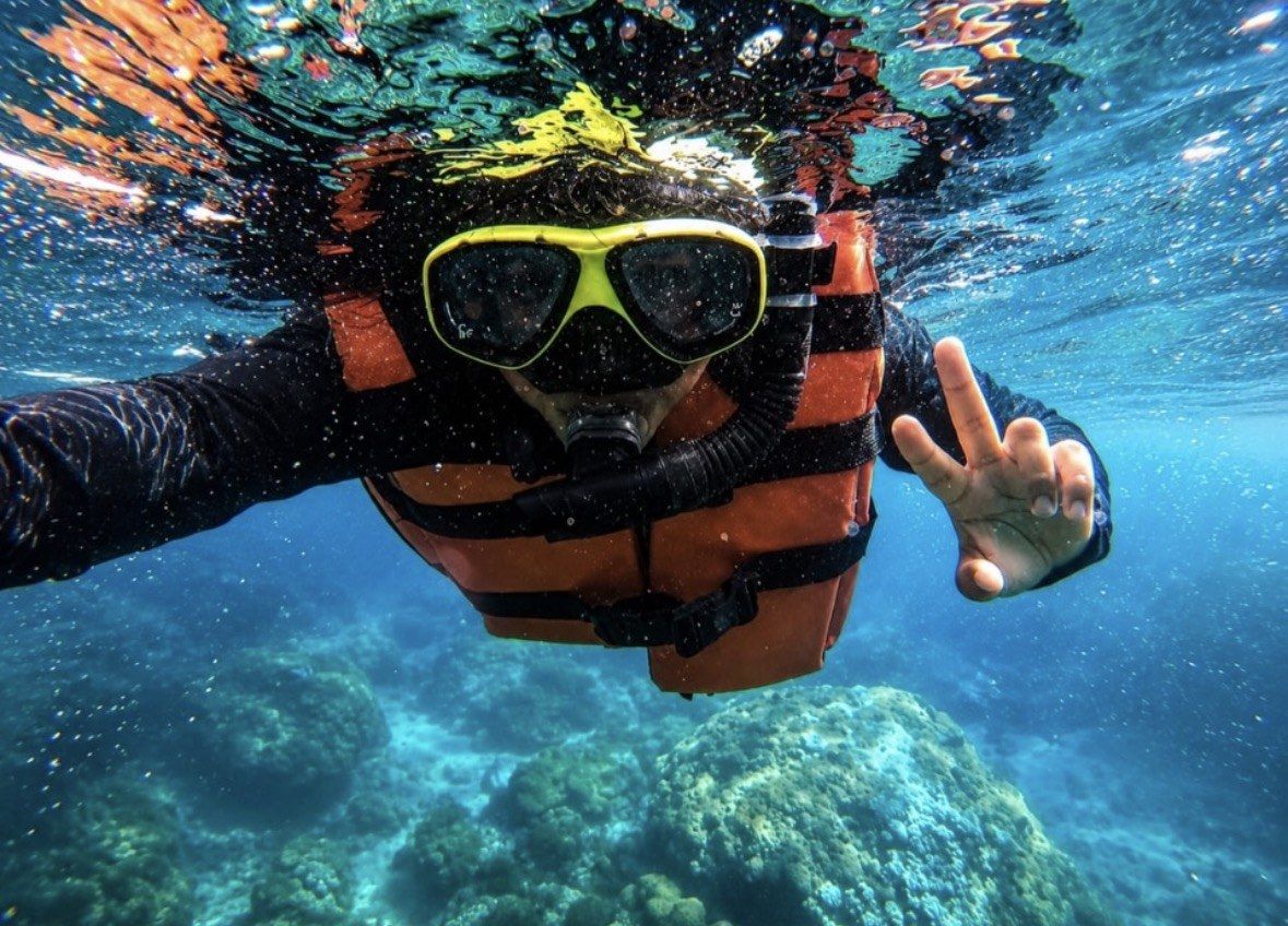 Snorkeler in orange life vest and yellow mask gesturing beneath the surface