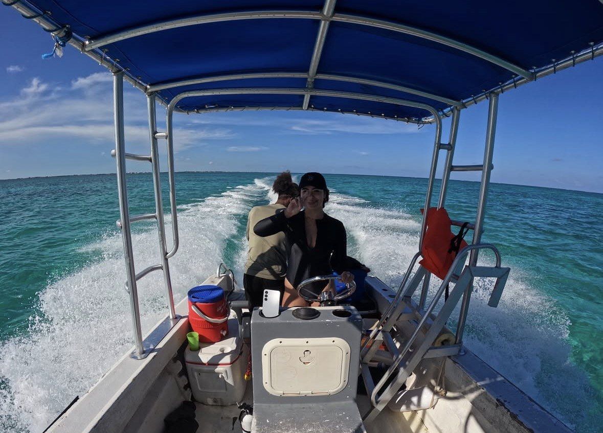 Two people steering a small awning-covered boat across open sea under blue sky